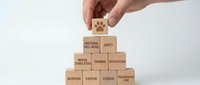 Hand placing wooden block with paw print on pyramid of workplace safety and mental health concept blocks on white background.