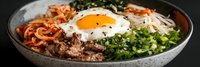 Korean bibimbap bowl with marinated beef, sunny side up egg, kimchi, bean sprouts, green onions and rice in gray ceramic bowl, panoramic food banner.