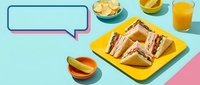 Club sandwich triangles on yellow plate with chips, pickle, and orange juice on colorful background with speech bubble copy space.