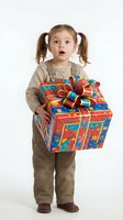 Young Caucasian girl with pigtails holding colorful wrapped gift box with ribbon bow, expressing surprise and joy, isolated on white background for holiday and celebration designs.