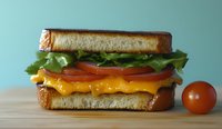 Fresh grilled cheese sandwich with melted cheddar, crisp lettuce, ripe tomato slices on toasted bread, served on wooden surface against blue background.