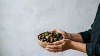 Close-up of male hands holding wooden bowl filled with mixed olives, featuring green and black varieties. Perfect for food, culinary, Mediterranean cuisine, healthy eating, and restaurant marketing projects.