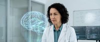 Middle-aged woman with dark curly hair and olive complexion wearing white lab coat over teal shirt, standing in modern laboratory setting with glowing blue brain hologram visualization displayed beside her, representing neuroscience research and medical innovation.