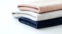 Neatly folded stack of soft cotton towels in pink, gray and navy blue colors on white background, showing texture and layers for bathroom or spa decor.