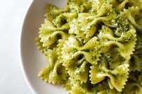Fresh farfalle pasta with vibrant green pesto sauce and parmesan cheese served in white bowl for Italian cuisine and homemade cooking concepts.