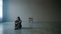 Sad young adult male sitting alone on floor in empty room with single chair, expressing loneliness, depression, mental health struggle, isolation and emotional distress for therapeutic or awareness content.