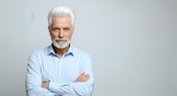Mature Caucasian man with white hair and beard wearing light blue shirt, arms crossed, isolated on white background for corporate and business use.