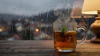Hot tea cup with mint on wooden table by rainy window creating cozy atmosphere for relaxation and comfort during stormy weather indoors.