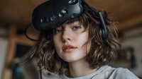 Young woman with curly hair wearing virtual reality headset in cozy indoor setting, exploring immersive technology.
