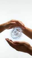 Hands of a person with medium skin tone cradling a transparent blue gear mechanism against a white background, symbolizing innovation, technology protection, and mechanical care for design projects.