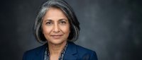 Confident South Asian senior businesswoman with gray hair in navy blazer smiling against dark studio background, professional headshot portrait.