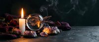 Mystical fortune telling setup with crystal ball, burning candle, dried roses and tarot cards on dark atmospheric background with smoke.