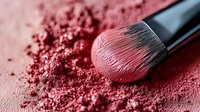 Makeup brush with pink blush powder scattered on surface, close up view showing soft bristles and cosmetic texture in professional beauty photography.