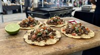 Fresh Mexican street tacos with seasoned ground beef, diced onions, cilantro and lime on corn tortillas served on wooden cutting board in restaurant kitchen.