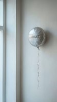 Silver foil balloon with text floating against white wall near window, suitable for retail marketing, sales promotions, and commercial advertising campaigns.