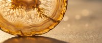 Vintage amber glass bowl with intricate pattern casting shadows on sandy beach surface with warm golden sunlight and soft bokeh background.