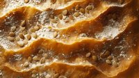 Macro shot of caramel dessert surface with salt crystals scattered across wavy golden layers creating rich texture and depth for food photography and design.