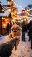 Hand holding paper cone filled with roasted chestnuts at festive winter market with warm bokeh lights creating cozy holiday atmosphere.
