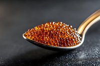 Red caviar pearls on silver spoon against dark background, macro shot highlighting luxurious texture and amber color of salmon roe in gourmet presentation.