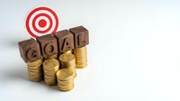 Wooden blocks spelling GOAL with golden coins and red target symbol representing financial planning success and achievement motivation for business growth.