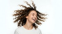 Young mixed-race woman with curly hair laughing joyfully with hair flowing in motion against white background isolated for design use.
