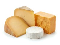 Assorted cheese wedges and round white cheese wheel isolated on white background, featuring aged cheddar and soft varieties for culinary and food styling use.