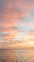 Serene ocean horizon at golden hour with soft pink and orange clouds reflecting on calm water, ideal for travel and nature backgrounds.