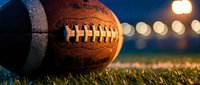 American football on grass field with stadium lights creating bokeh background during evening game time.