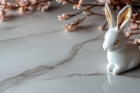 White ceramic bunny figurine with gold accents on marble surface with pink cherry blossom branches creating soft spring atmosphere for Easter decor and celebrations.