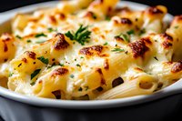 Creamy baked pasta shells with melted cheese sauce and fresh herbs garnish served on white plate against dark background, close up view of homemade comfort food.