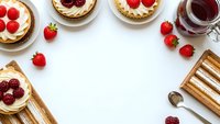 Delicious berry tarts with cream filling arranged on white background with fresh strawberries, raspberries and tea cup creating elegant dessert frame.
