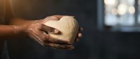Baker hands holding fresh bread dough in warm kitchen light. Artisan baking process with flour-dusted fingers kneading homemade pastry preparation.