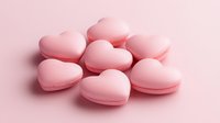 Heart shaped pink macarons arranged on soft pink background, sweet romantic dessert composition for Valentine's Day, wedding or anniversary celebration.