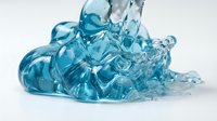 Spilled blue gel or liquid substance with splashing droplets and flowing waves on white background, suitable for cosmetics, skincare, cleaning products, and wellness packaging design.