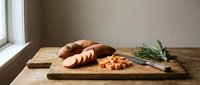 Freshly baked bread loaf sliced on wooden cutting board with cheddar cheese cubes and fresh rosemary sprigs, ideal for food styling, culinary blogs, and recipe content.