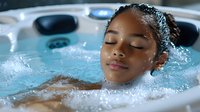Young African American woman relaxing in bubbling hot tub with eyes closed, enjoying spa hydrotherapy treatment. Wellness and stress relief concept.