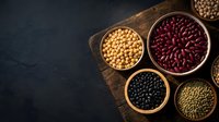 Assorted legumes and beans in wooden bowls on rustic cutting board, featuring kidney beans, soybeans, black beans and lentils for healthy cooking.