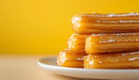Stack of fresh churros with sugar coating on white plate against yellow background, close up view showing crispy texture and sweet dusting.