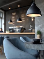 Modern industrial cafe interior with black pendant lights, gray upholstered chairs and concrete table. Contemporary restaurant design with warm lighting atmosphere.