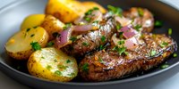 Juicy grilled steak medallions with golden potatoes and red onions on dark plate, garnished with fresh herbs and butter sauce, close-up food photography.