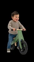 Happy toddler boy riding a green wooden balance bike, isolated on transparent background, cut out for stickers, print on demand, T-shirt design, and clipart use.