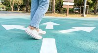 Person in jeans and sneakers standing on turquoise basketball court with white directional arrows painted on ground for sports and recreation activities.