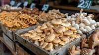 Fresh organic mushrooms displayed in wooden crates at farmers market, including honey fungus and white button varieties arranged in rustic style for retail sale.