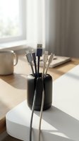 Multiple charging cables organized in black cylindrical holder on modern desk workspace with laptop and coffee mug in soft natural lighting.