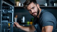 Young Caucasian male technician with beard in dark uniform repairing dishwasher in modern kitchen. Professional maintenance and repair service concept.