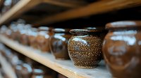 Handcrafted clay pottery on wooden shelves in workshop, traditional ceramic vases with textured surface pattern in warm brown tones, selective focus on detailed pot.