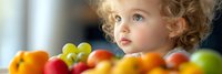 Adorable blonde toddler girl with curly hair looking at colorful fresh fruits on table. Healthy eating, nutrition education for children concept.