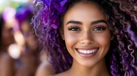 Young woman with vibrant purple curly hair smiling brightly at camera, showing white teeth and natural makeup against blurred background. Positive expression and modern style.