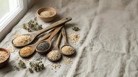Assorted organic grains and seeds in wooden spoons on linen fabric for healthy cooking and nutrition concepts.