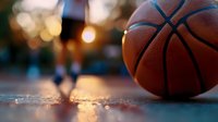 Basketball on outdoor court with warm evening lights and blurred players in background creating atmospheric sports scene for recreation and fitness concepts.